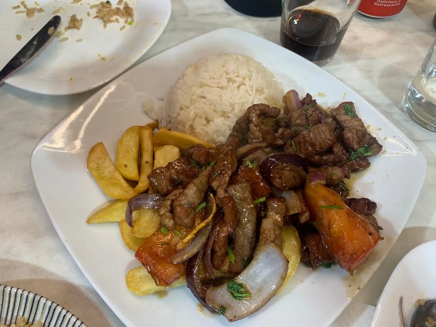 Lomo saltado con tiras de ternera, cebolla, tomate, patatas fritas y arroz blanco