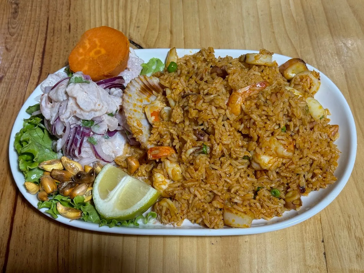 Fuente con ceviche, arroz con mariscos, cancha, boniato y limón sobre una mesa de madera