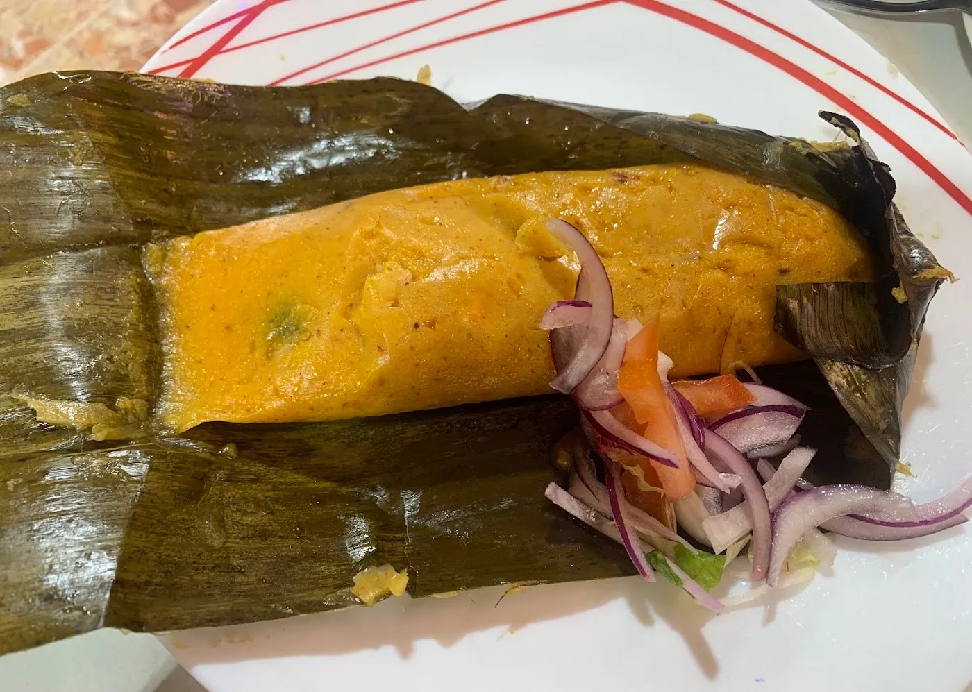 Tamal de masa de maíz amarilla sobre su hoja de plátano, con cebolla morada