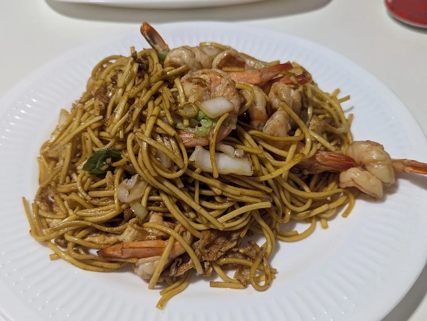 Tallarines salteados con gambas y verduras en un plato blanco