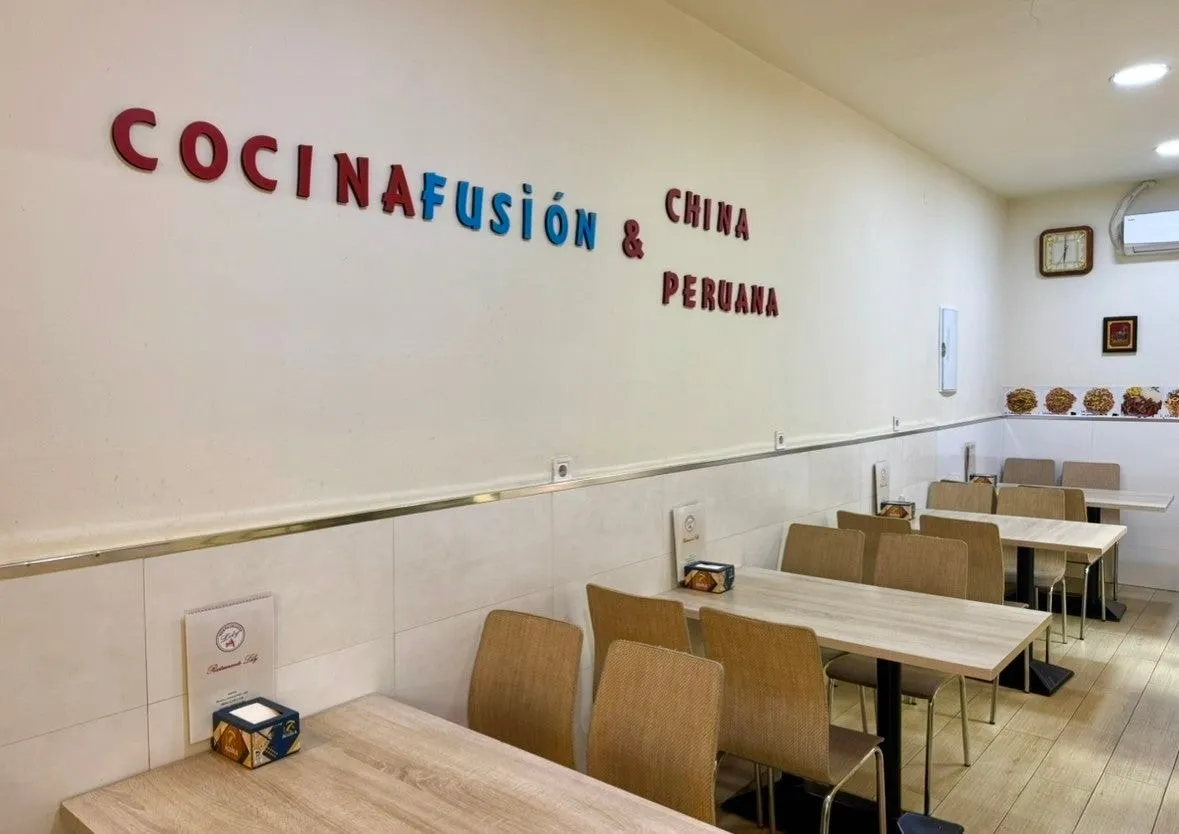 Comedor con mesas vacías y las letras «Cocina fusión china & peruana» en la pared