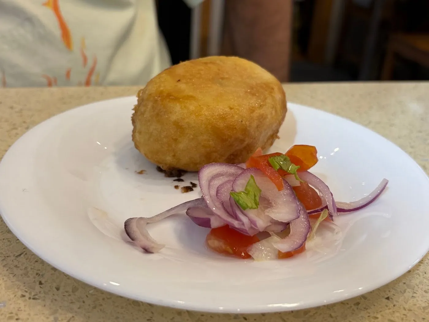 Papa rellena dorada con salsa criolla de cebolla y tomate en un plato blanco