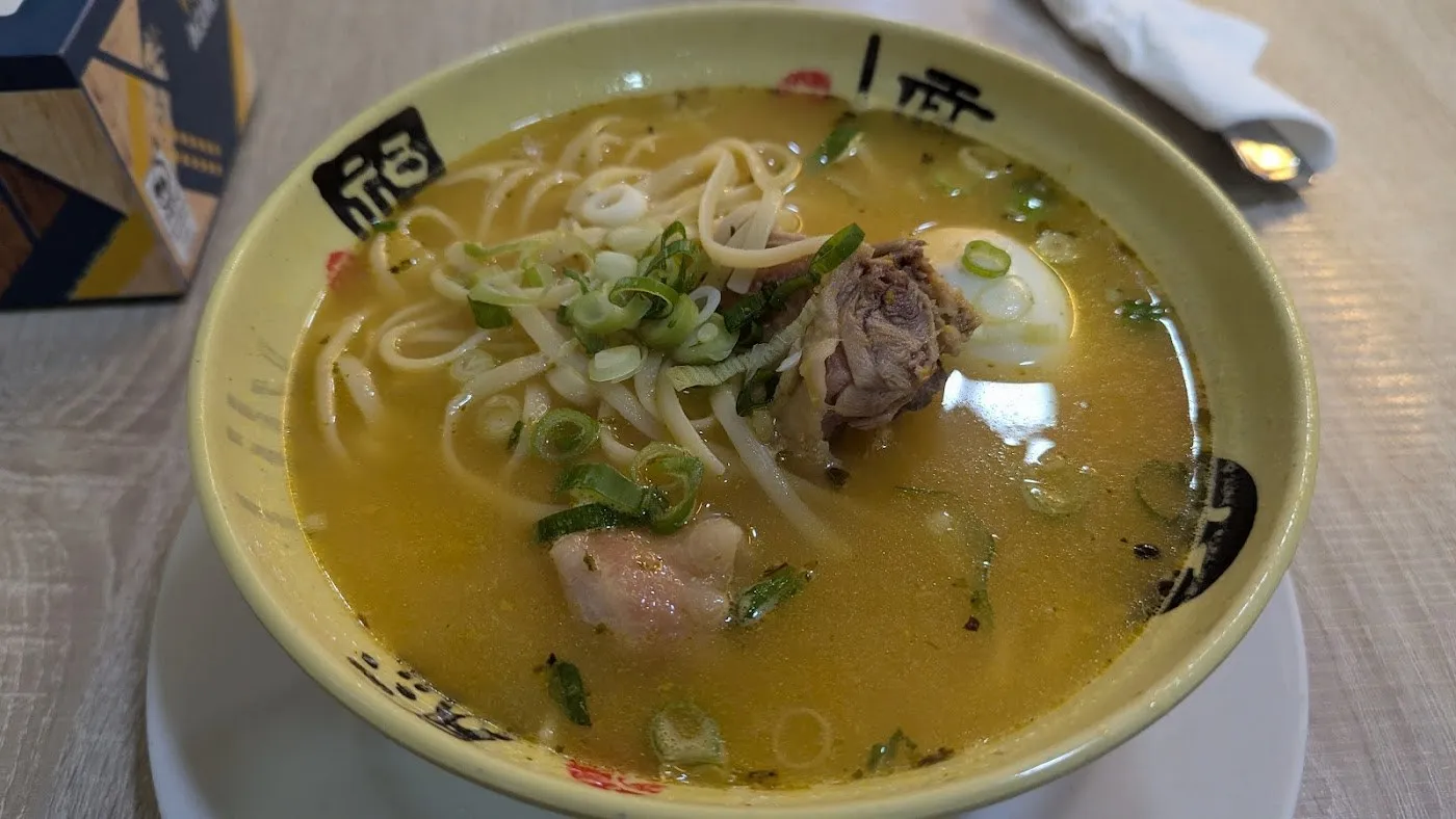 Caldo de gallina con fideos, huevo y cebolleta en un cuenco verde